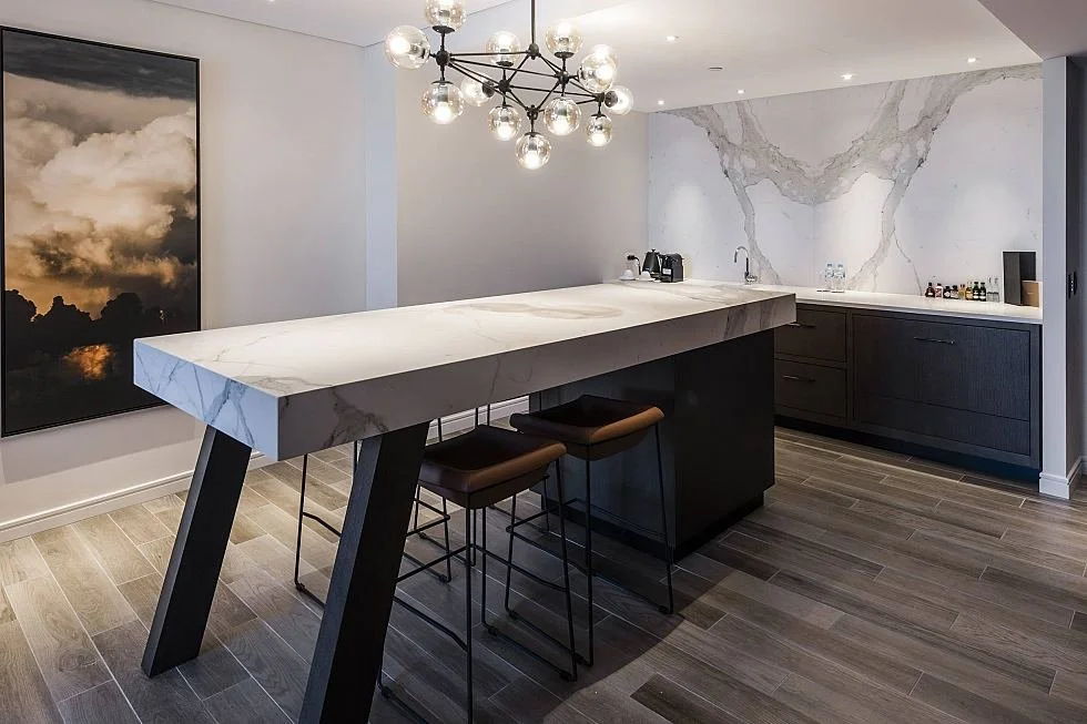Long kitchen island and stools beneath a branching chandelier.