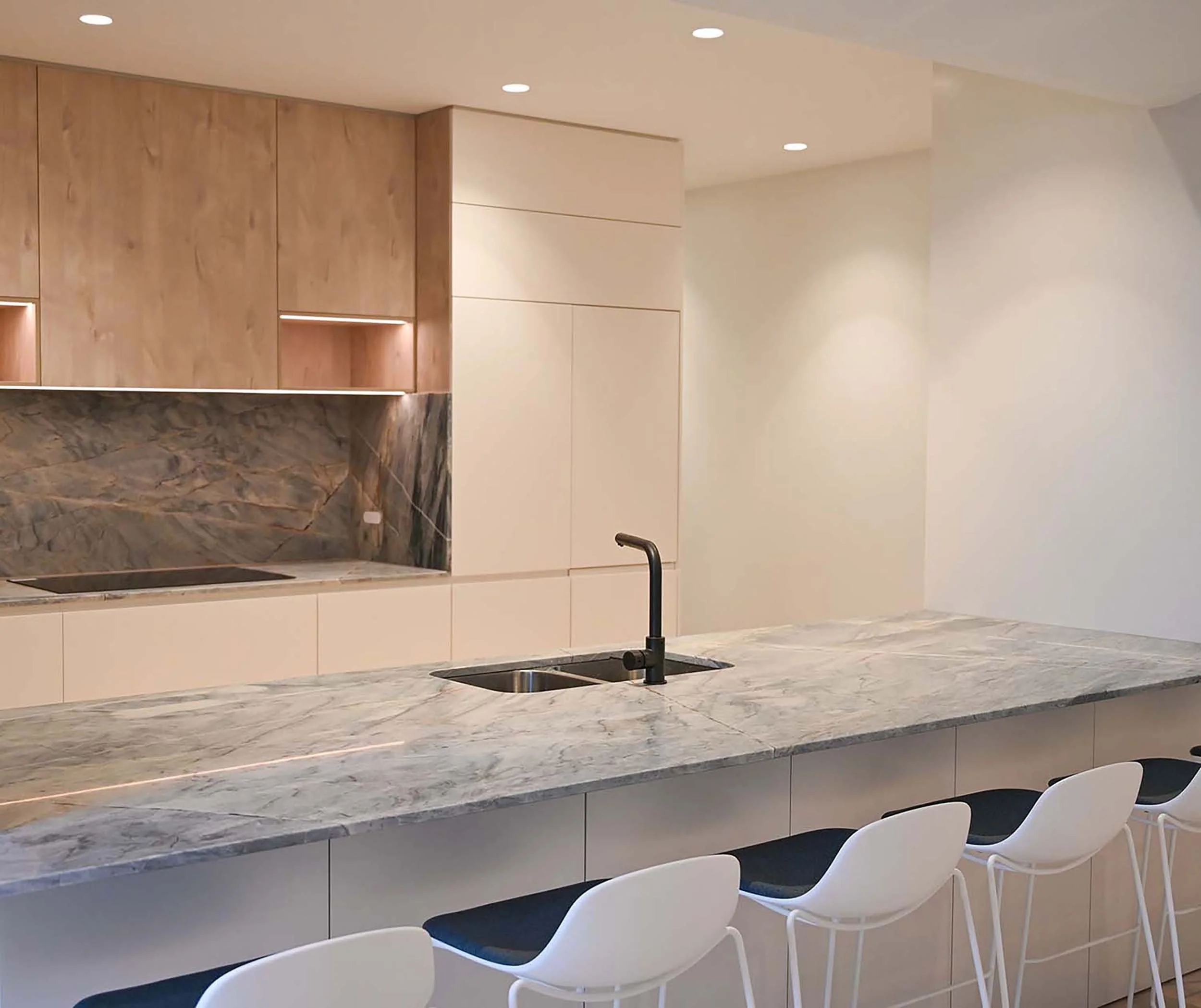 Modern kitchen with marble countertop, light wood and white cabinets, black sink faucet, and white chairs with dark cushions.