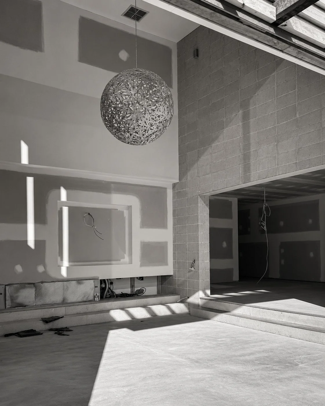 Lorde House living space under construction with sculptural pendant lighting and a fireplace wall.