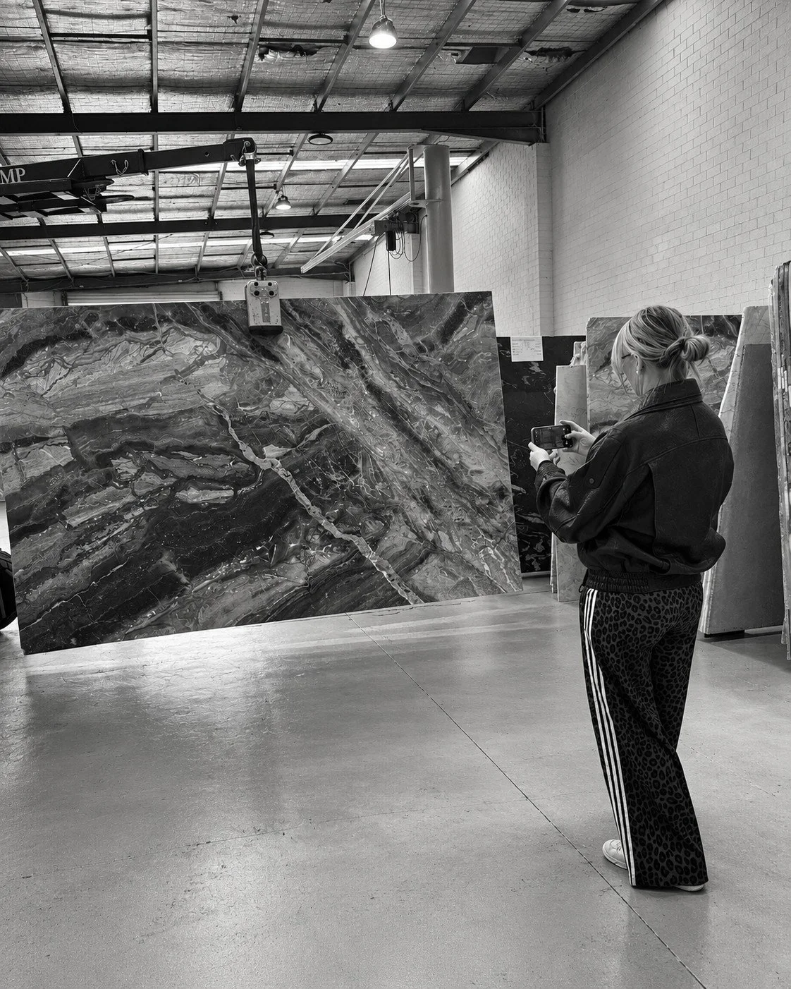 Alpine House material selection in a stone workshop, with a designer reviewing a richly veined natural stone slab.