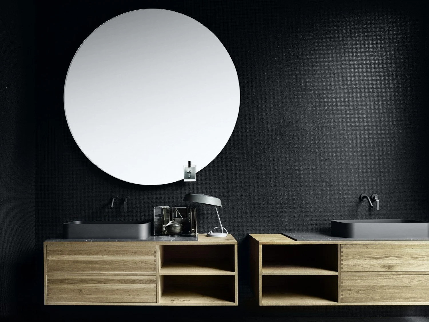 Large round mirror above twin timber-front bathroom vanities against a dark wall.