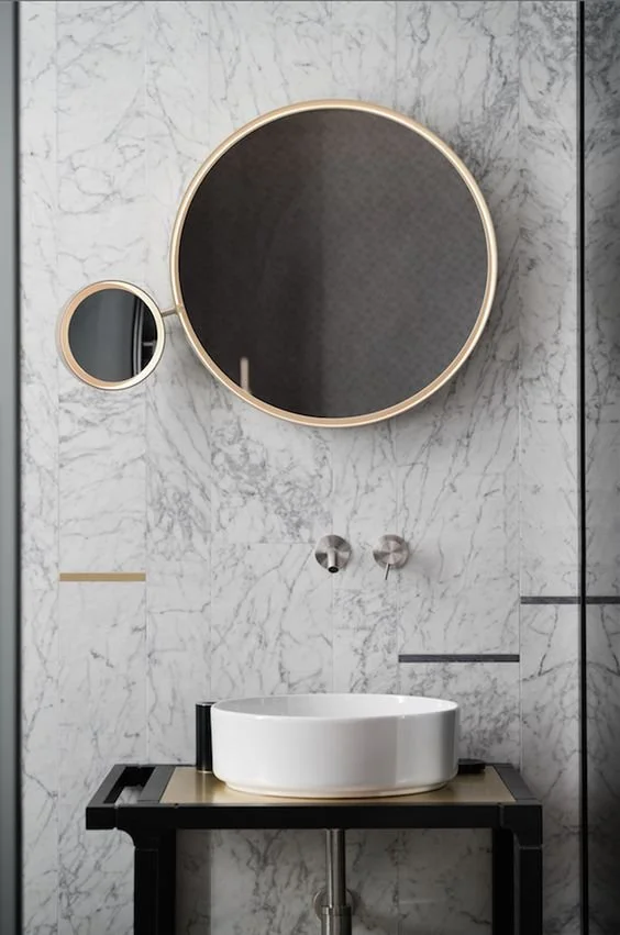 Round mirror and white vessel basin against grey stone bathroom walls.