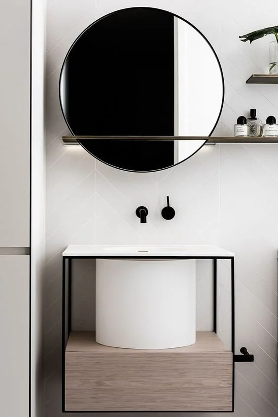 Round black-framed mirror above a pale basin and timber bathroom vanity.