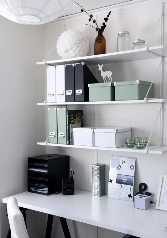 Open white shelving displaying kitchenware above a compact desk.