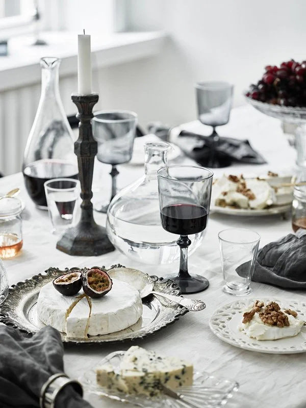 Table setting with layered plates, dark glasses and a tall candleholder.