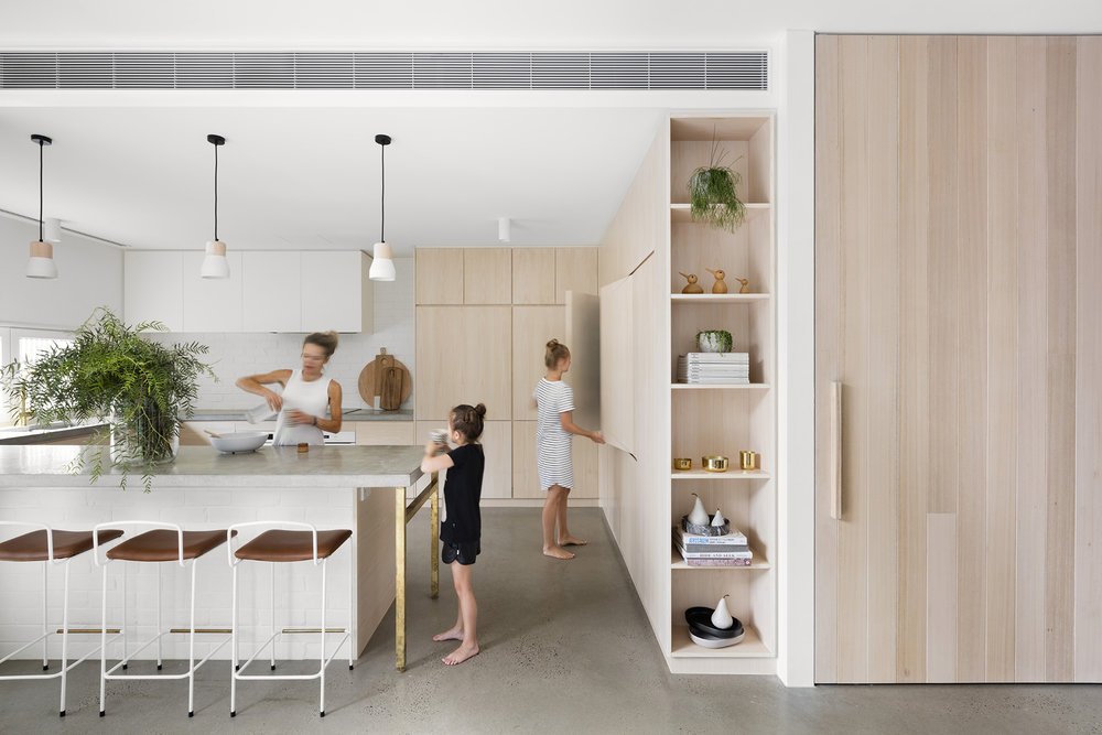 Family kitchen with pale timber cabinetry, an island and white stools.