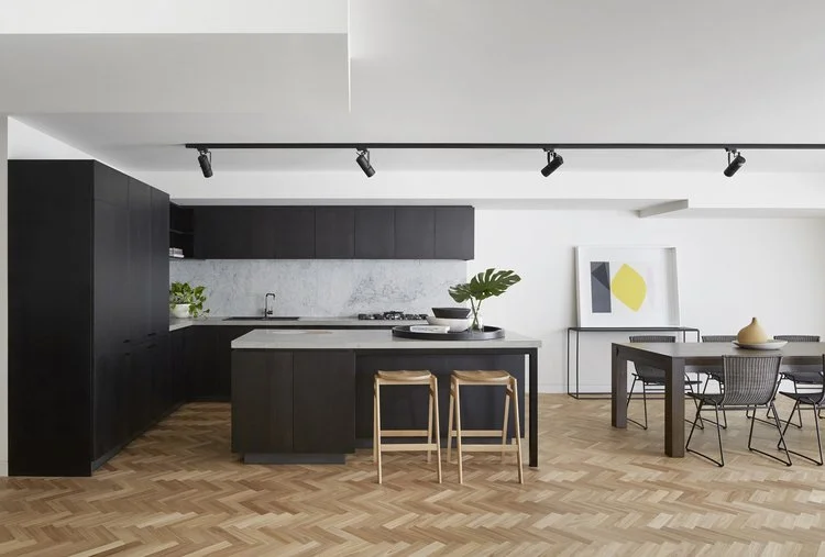 Dark kitchen island and cabinetry beside a dining area with parquet flooring.