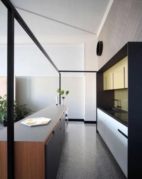 Long kitchen with timber cabinetry, a grey island and black-framed glazing.