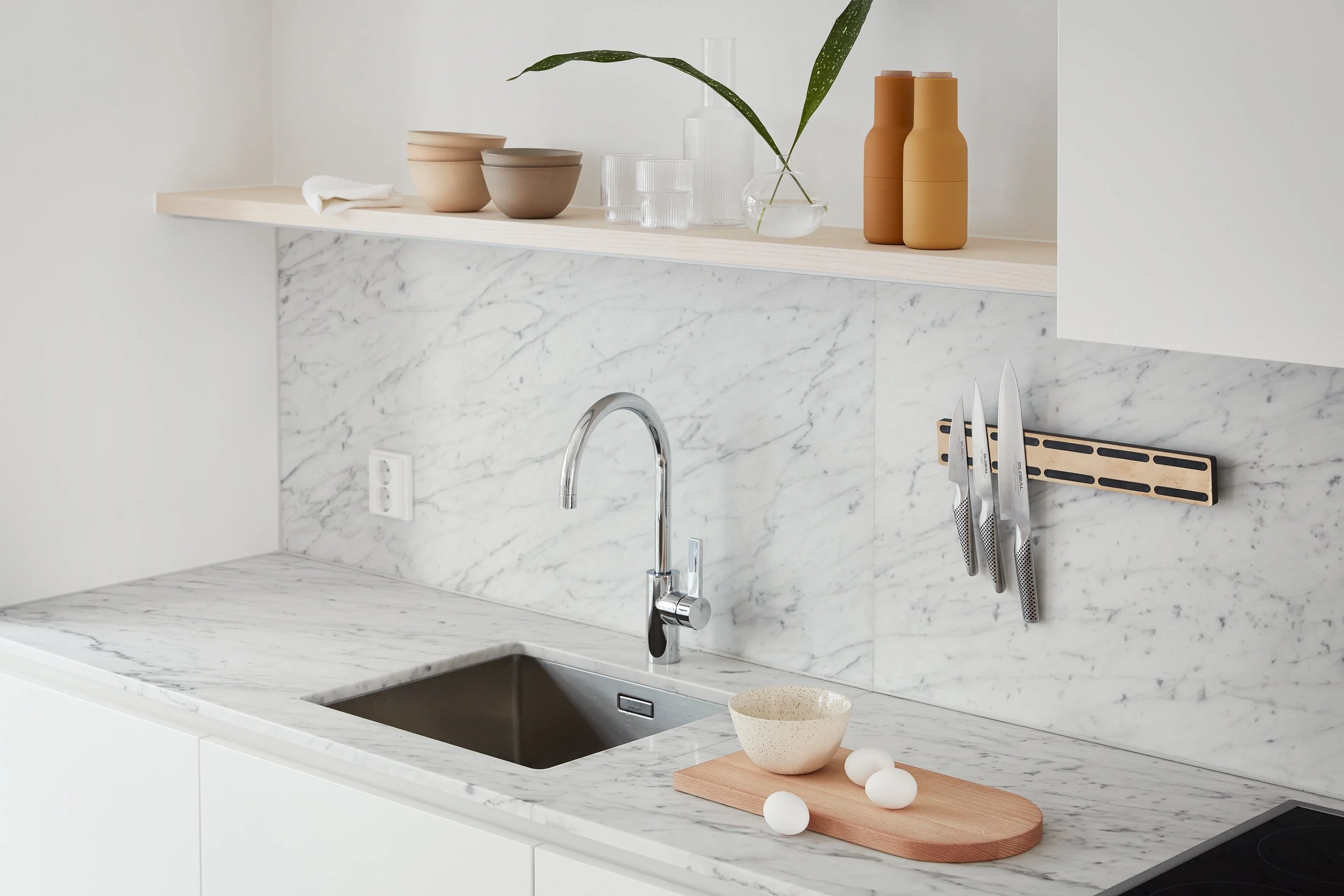Pale veined stone sink bench with a curved chrome tap and open display shelf.