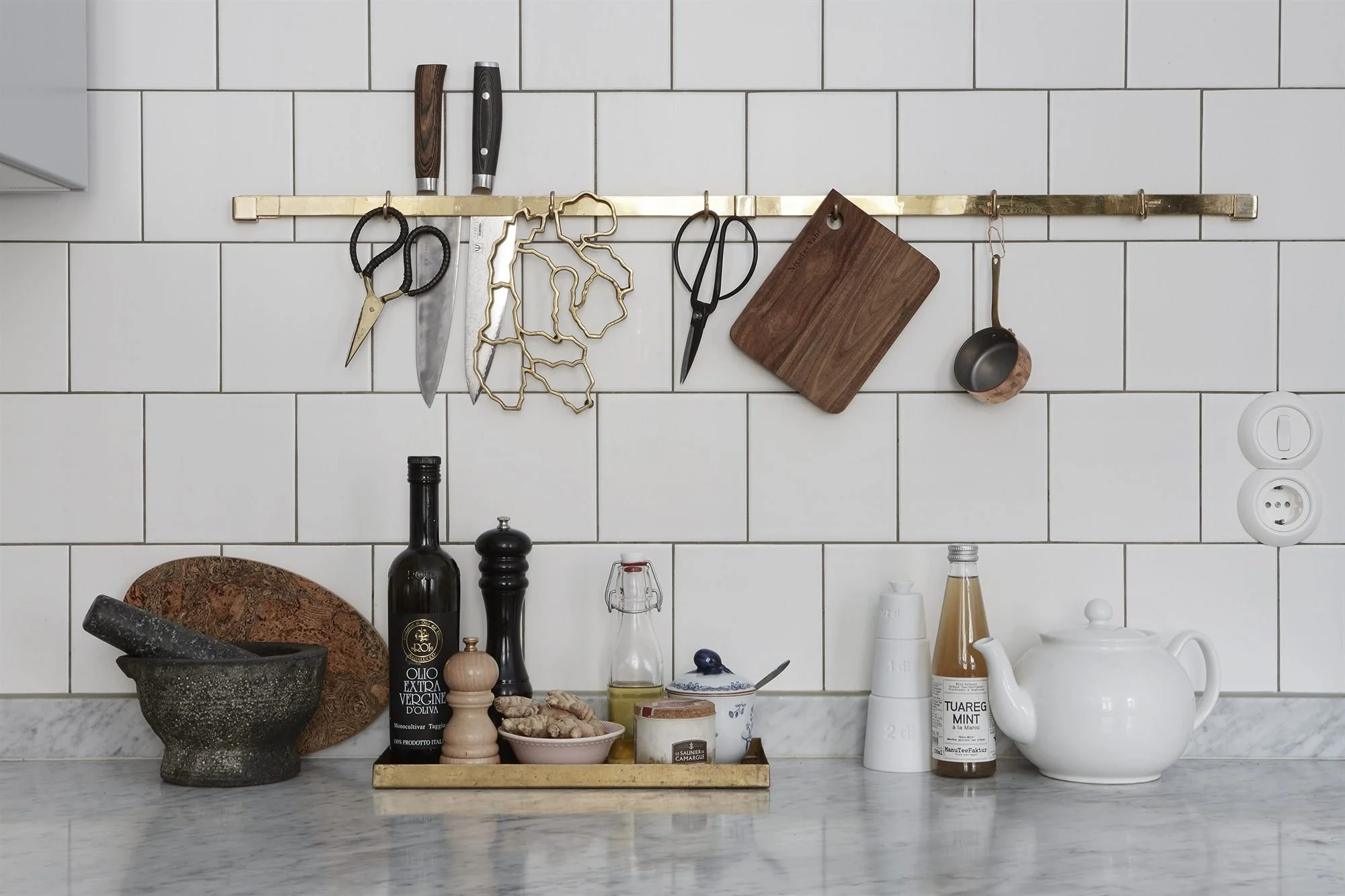 Utensils and cutting boards hanging from a brass-toned rail against white tiles.