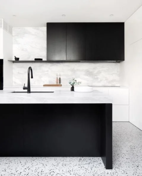 Black kitchen cabinetry and pale stone surfaces with a curved dark tap.
