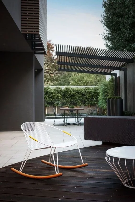 Outdoor lounge area with white chairs beneath a timber pergola.