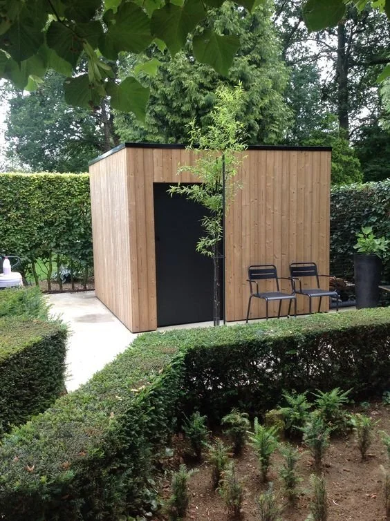 Timber-clad garden room surrounded by trees and planted borders.