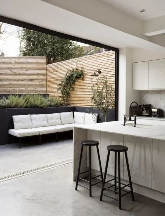 Kitchen island beside wide glazing opening to a courtyard seat and planted wall.