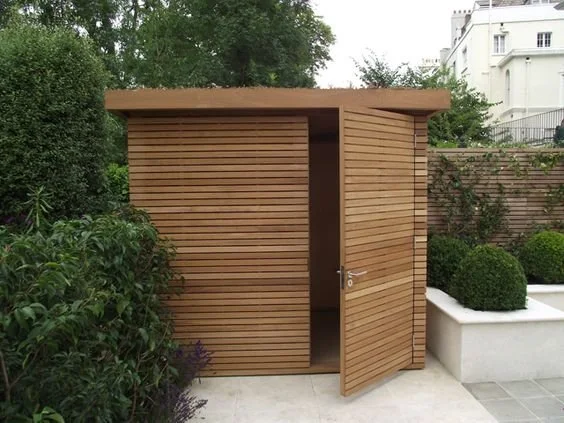 Small timber garden structure beside a hedge and curved garden wall.