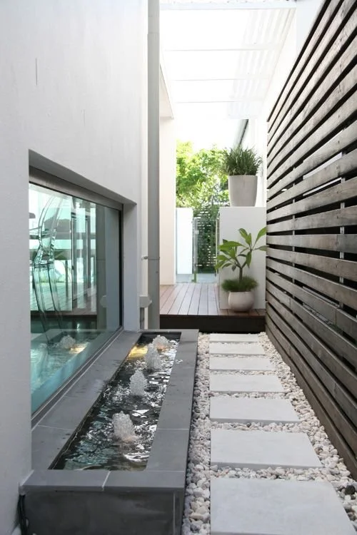 Narrow courtyard with stepping stones, glazing and dark horizontal cladding.