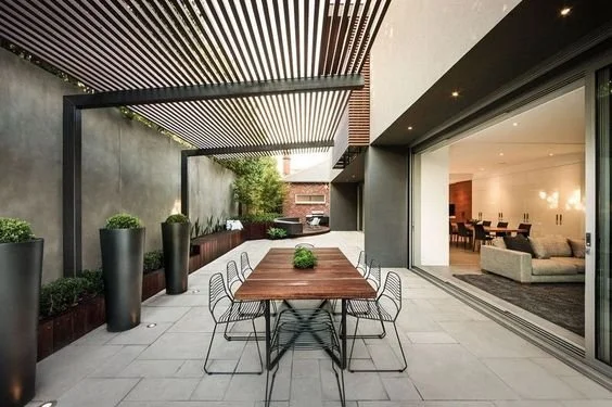 Covered outdoor dining area beneath a slatted pergola beside an open kitchen.