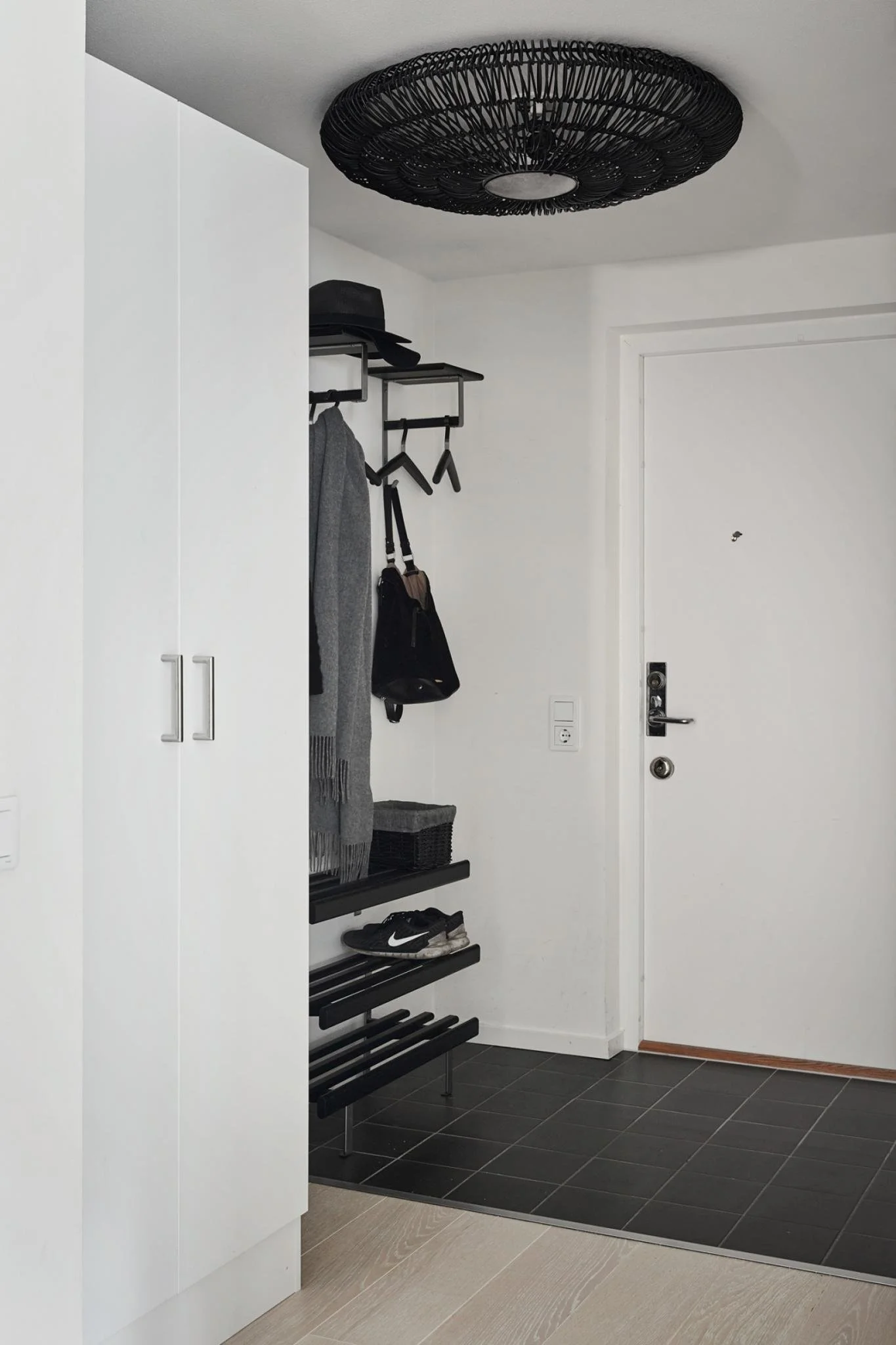 Entryway with open coat storage beside white cabinetry and a dark ceiling light.