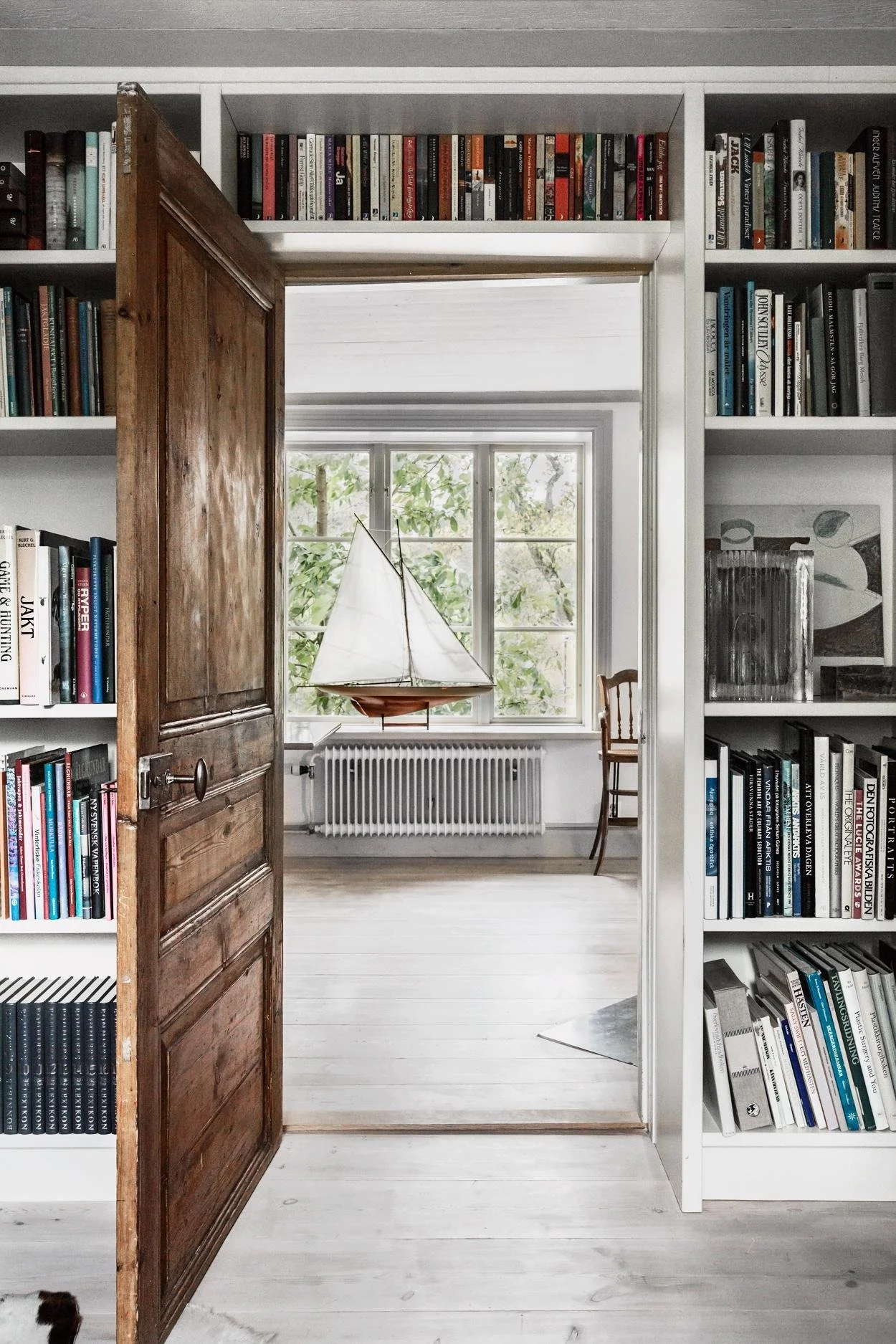 Doorway framed by full-height bookshelves leading to a bright room.