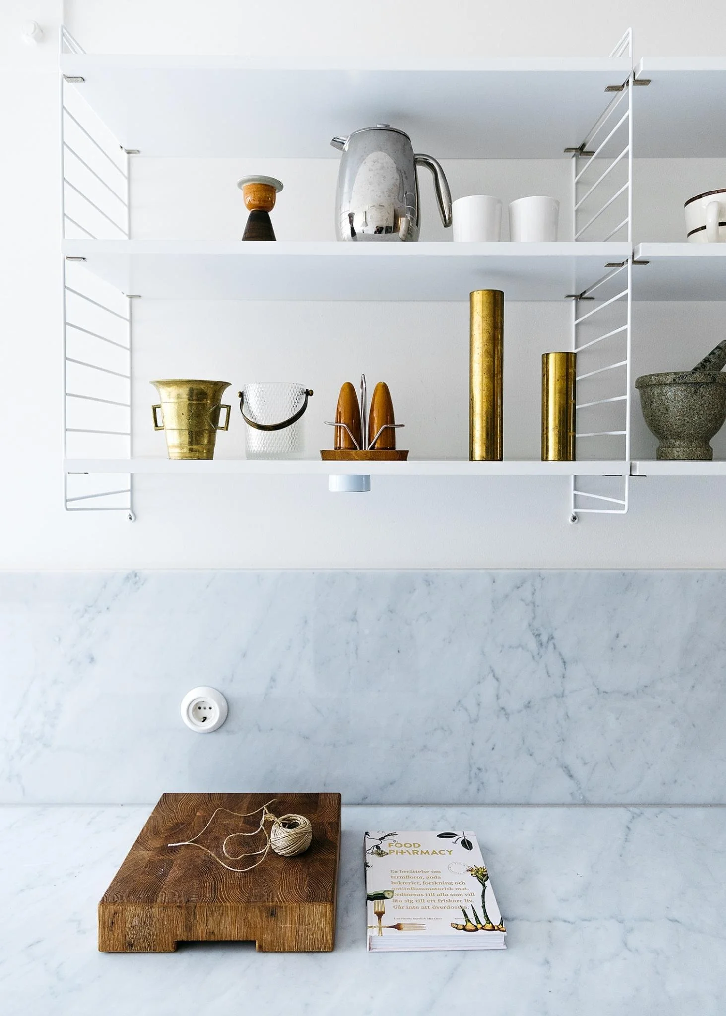 Open white kitchen shelving displaying ceramic vessels and books.