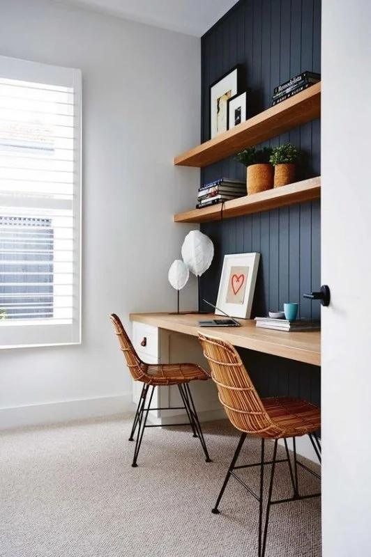 Built-in timber desk and shelving against a dark wall beside a window.