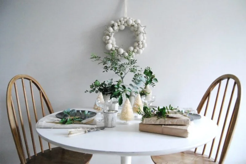 Round dining table with timber chairs, greenery and a wall wreath.