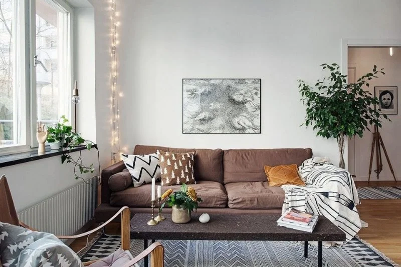 Tan sofa in a light room with plants and framed monochrome artwork.