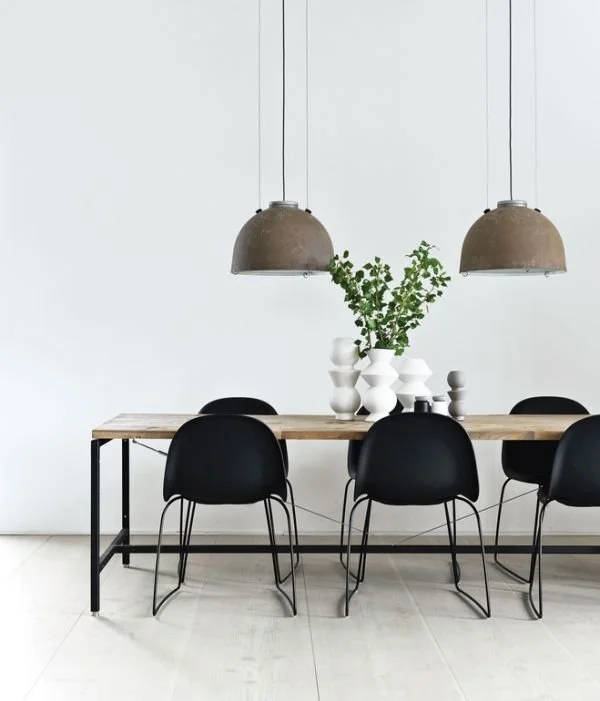 Minimal dining table with black chairs beneath two dome pendant lights.