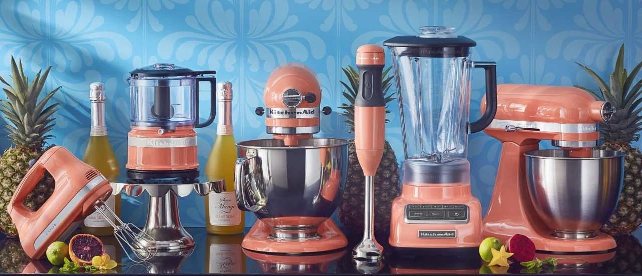 Coral-coloured kitchen appliances arranged against a blue tropical backdrop.