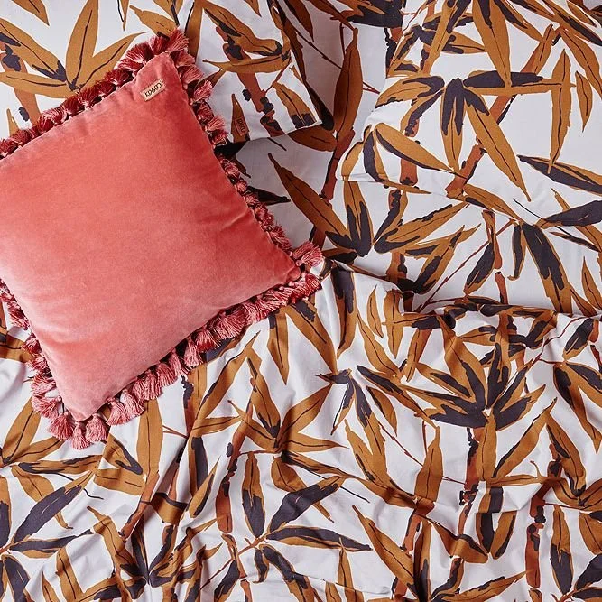 Coral cushion on bedding with a repeating botanical pattern.