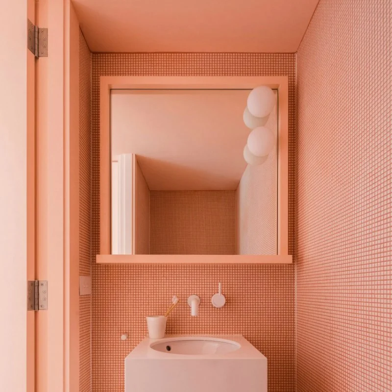 Coral-toned bathroom with a white basin beneath a rectangular mirror.