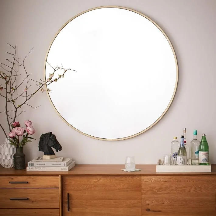 Large round mirror above a timber console with flowers and small objects.