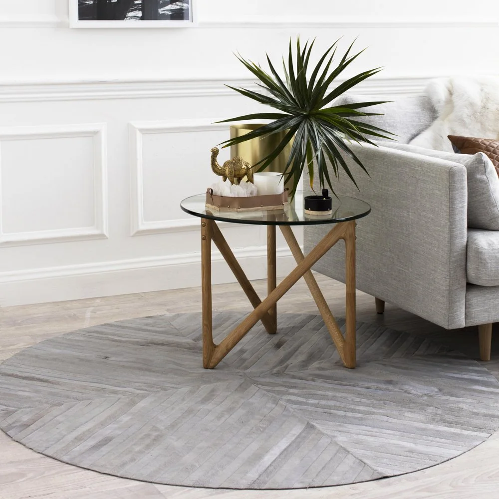 Round timber side table with a plant beside a grey armchair.