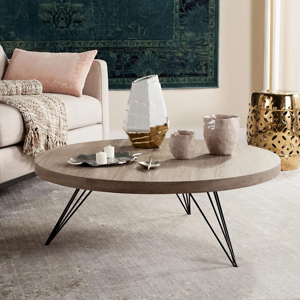 Round timber coffee table with dark angled legs beside pale seating.