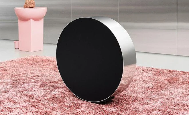 Circular dark side table with a reflective edge on a pink rug.