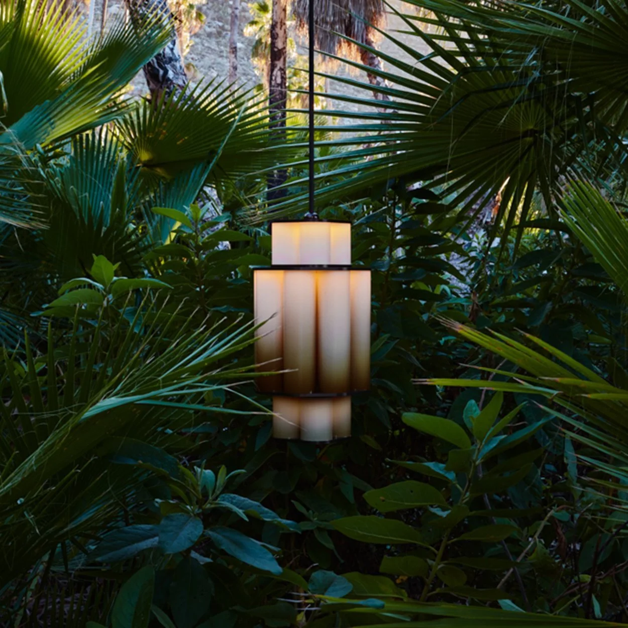 Warm cylindrical outdoor lamp nestled among green foliage.