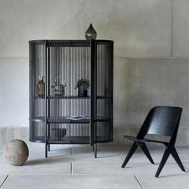 Dark glazed cabinet and sculptural black chair against a textured grey wall.