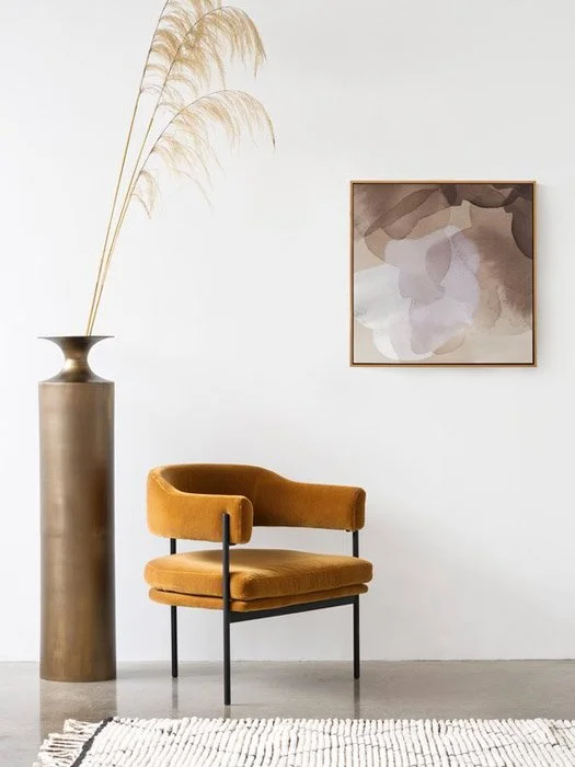 Mustard upholstered chair beside a tall vase and framed art.