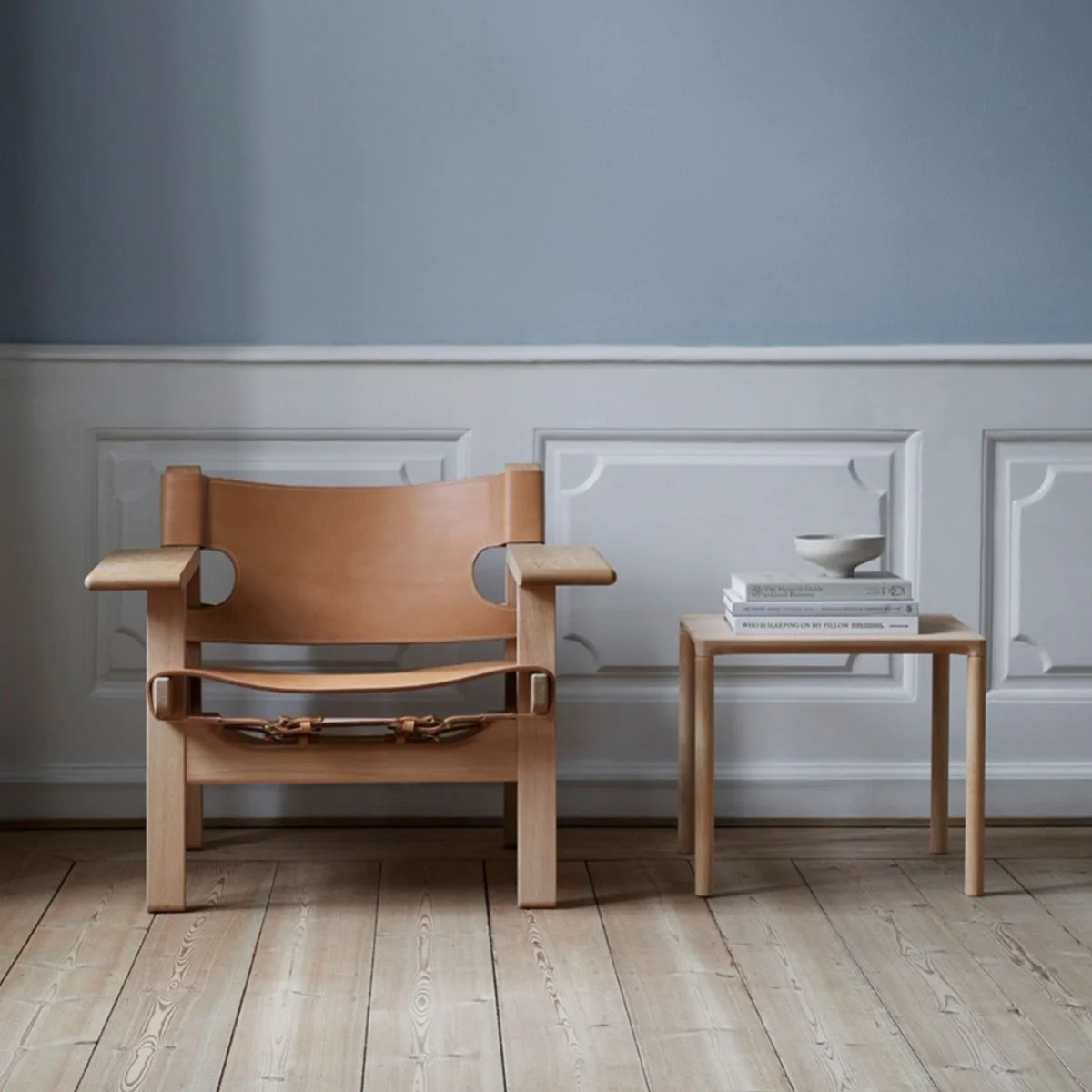 Tan lounge chair and side table against blue-grey wall panelling.