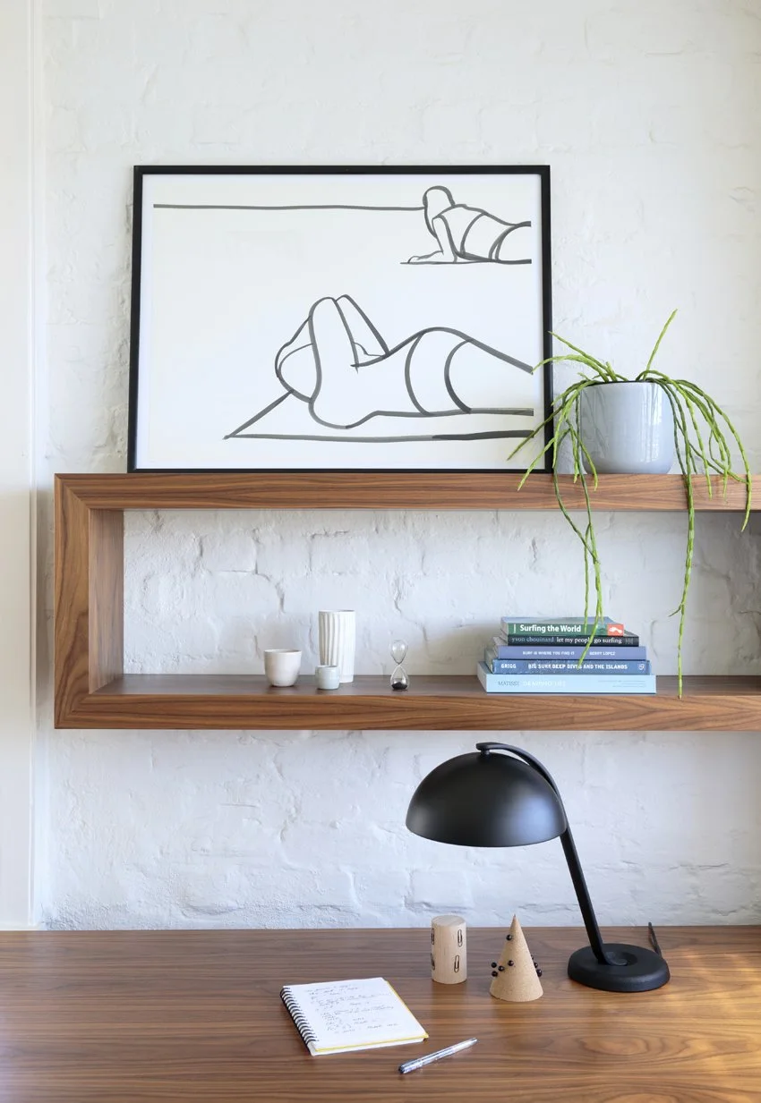 Timber wall shelving beneath a framed line drawing and small plant.