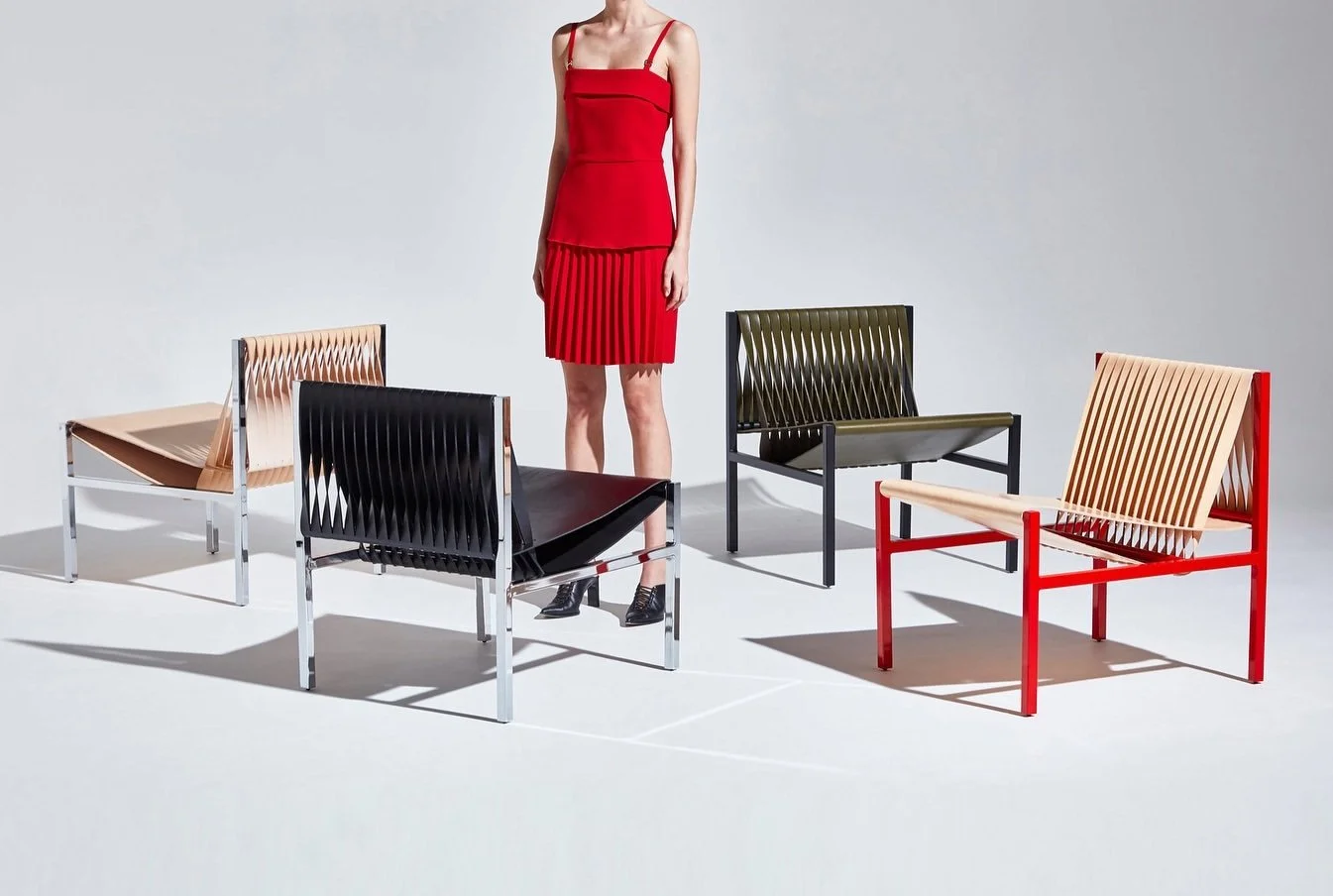 Woven lounge chairs with differently coloured metal frames beside a standing model.