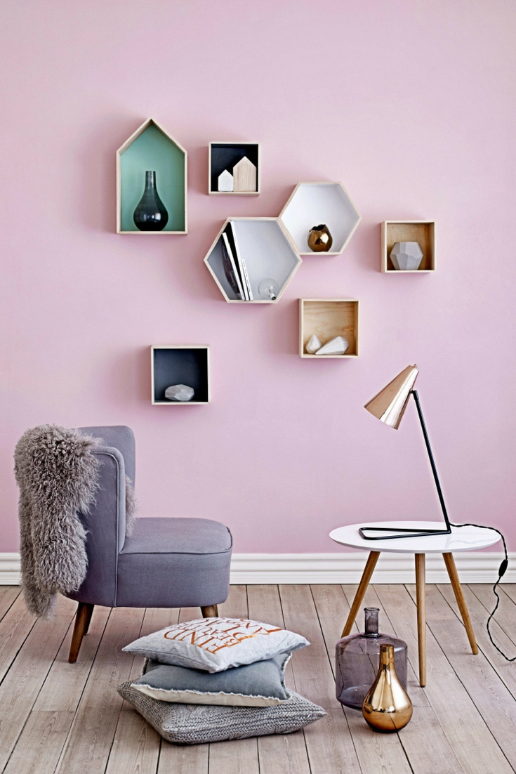 Pink living room wall with small geometric shelves, a grey chair and pale coffee table.