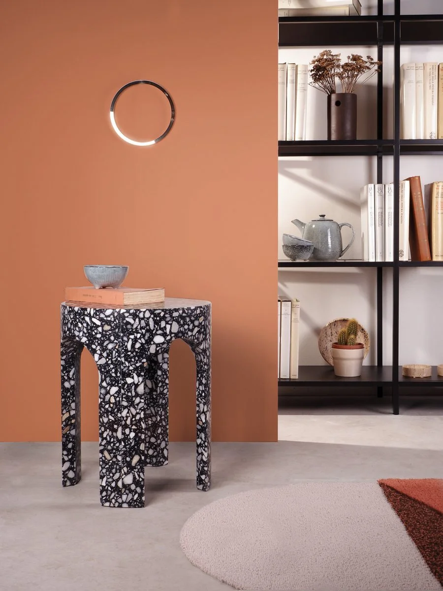 Terrazzo-patterned side table against a coral wall beside open shelving.