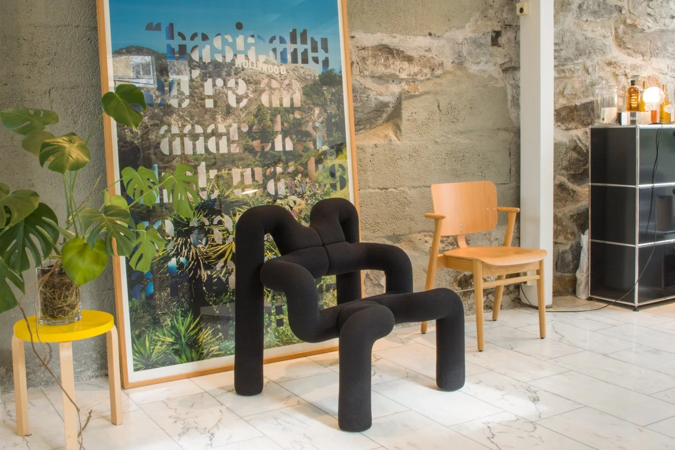 Black sculptural Ekstrem armchair in a room with stone walls, plants and framed art.