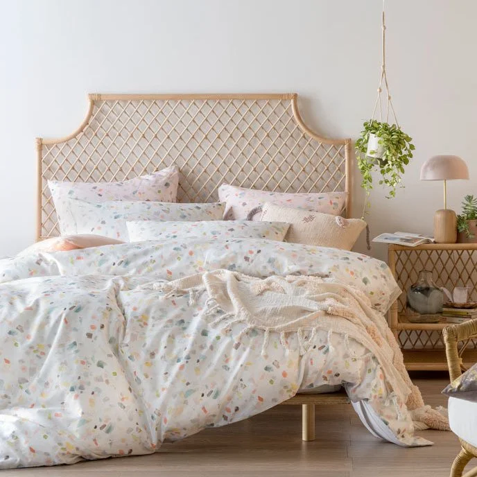 Soft floral bed linen against a woven bedhead beside a small timber cabinet.