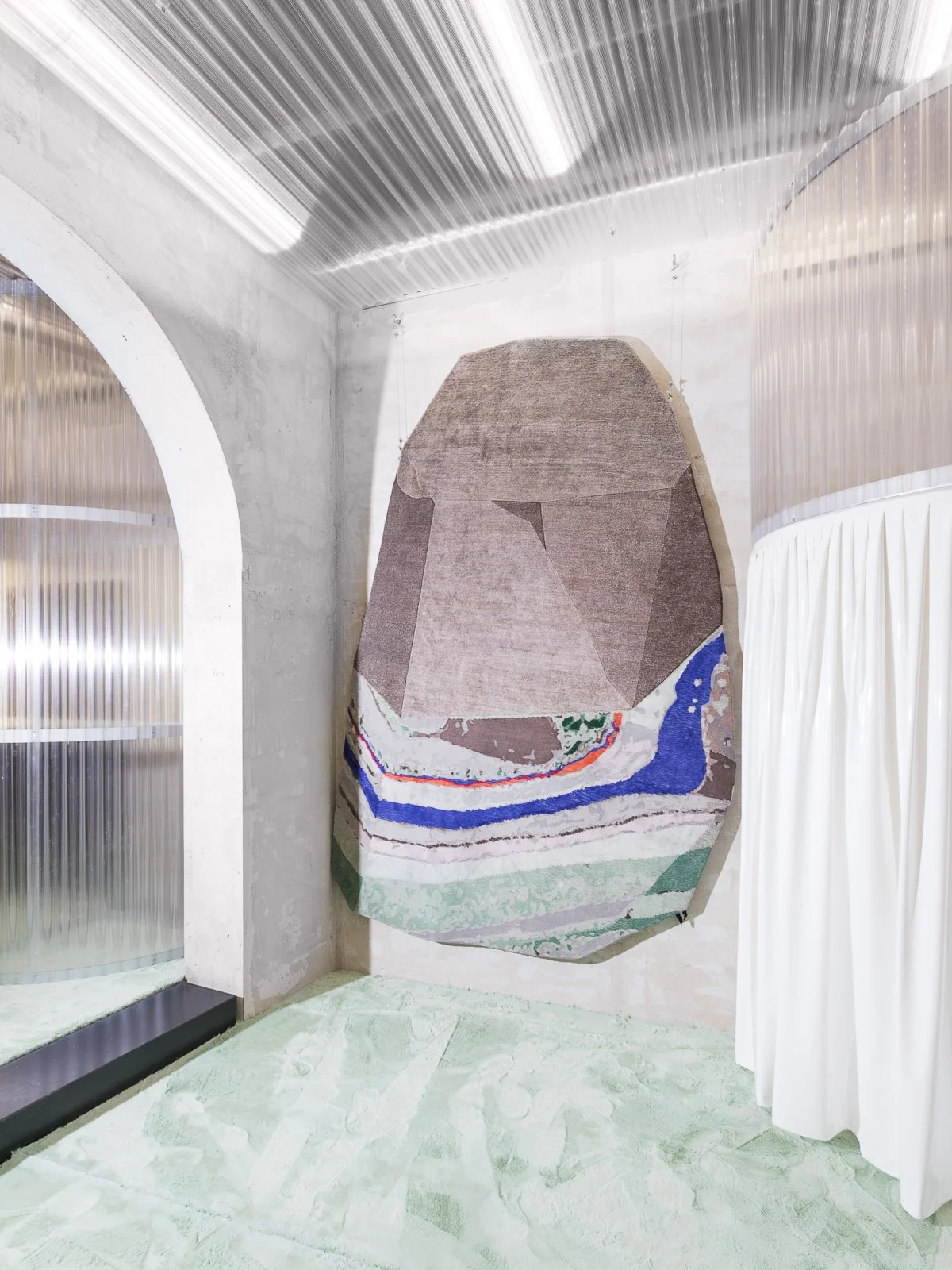 Sculptural rug with layered bands of colour displayed within an arched interior.