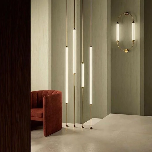 Slender suspended lighting tubes beside a rust-toned chair and muted green wall.