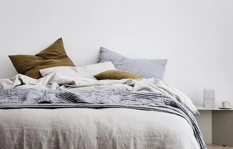 Pale layered bed linen with mustard and grey cushions.