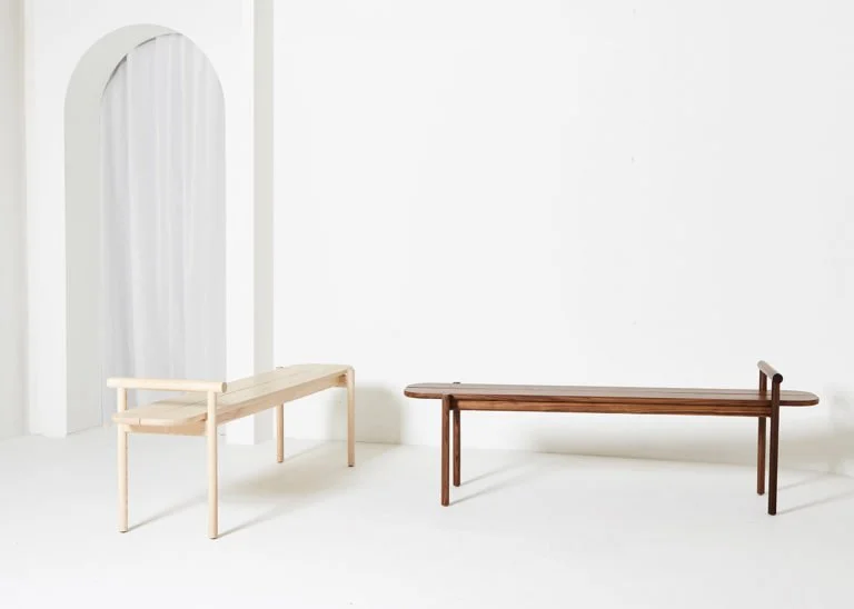 Arched standing mirror and slim timber bench displayed in a pale room.