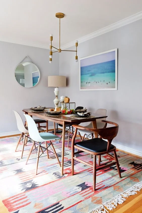 Dining table and chairs on a colourful patterned rug beneath a pendant.